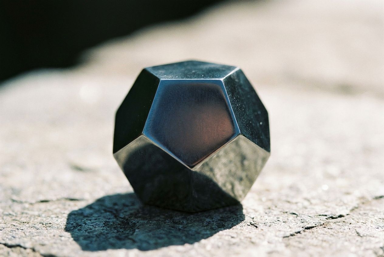 A striking close-up photograph of a perfectly crafted, polished dodecahedron, its twelve identical faces catching the light and casting intriguing shadows, emphasizing its geometric precision. The object is centered in a 3:2 landscape frame with a shallow depth of field, creating a sense of focus and mathematical elegance.