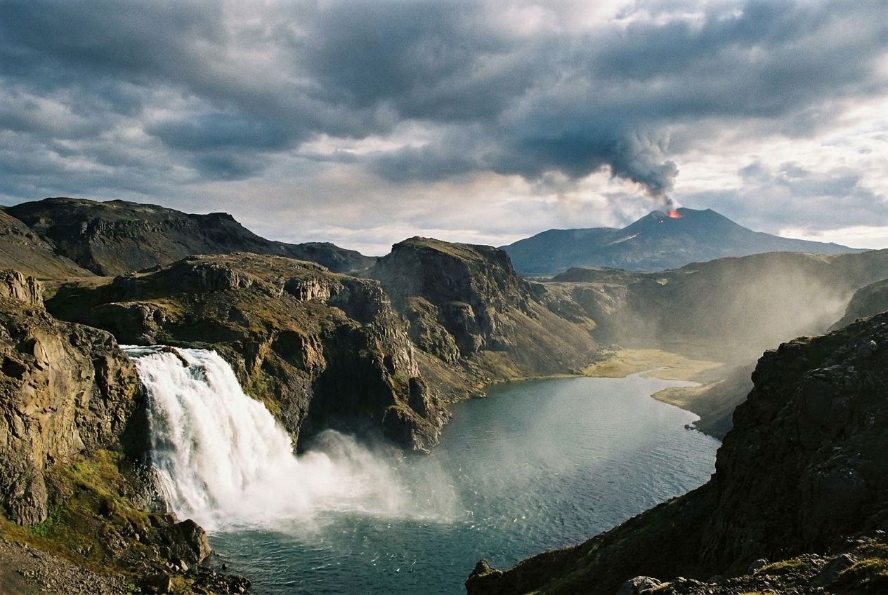 A majestic natural landscape photograph, composed for a 3:2 landscape frame, where all four elements are prominently featured: a powerful waterfall cascading into a serene lake, surrounded by ancient, rugged mountains, under a vast sky with dramatic clouds, and a distant, smoldering volcano on the horizon. The scene should convey a sense of primal energy and balance.