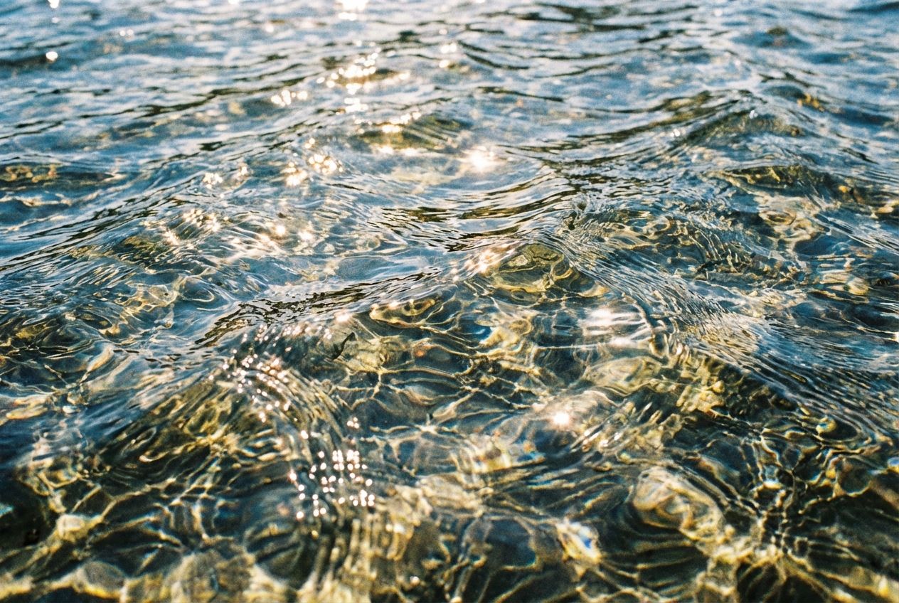 A close-up, wide-angle photograph of the surface of clear water, showing intricate patterns of ripples and small waves. Vibrant sunlight filters through the surface, creating dynamic refractions and reflections, emphasizing the movement and energy of the water, composed for a 3:2 landscape frame.
