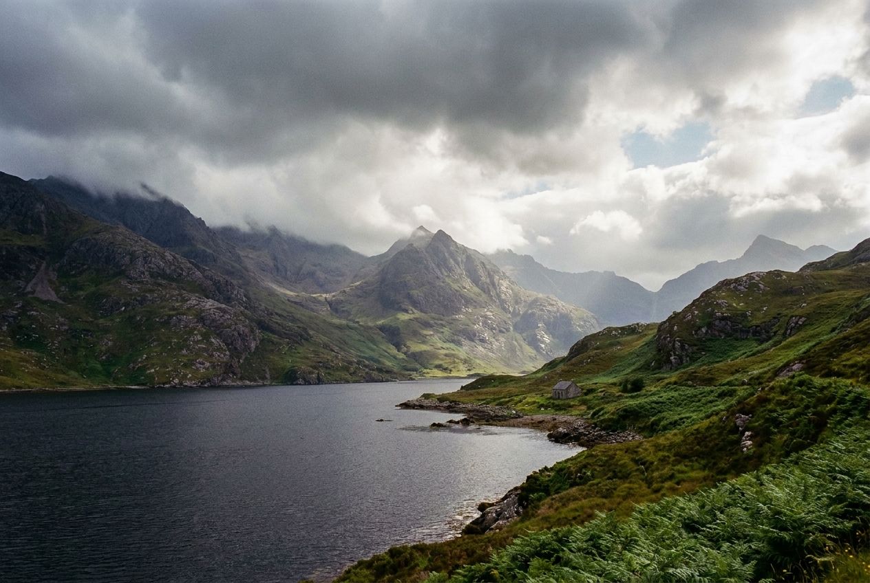 A dramatic, wide-angle photograph of a serene Scottish loch, with rugged, misty mountains rising majestically from its dark waters. The scene should convey the raw beauty of the Scottish Highlands, with hints of green foliage on the slopes, under a striking, cloudy sky, composed for a 3:2 landscape frame.