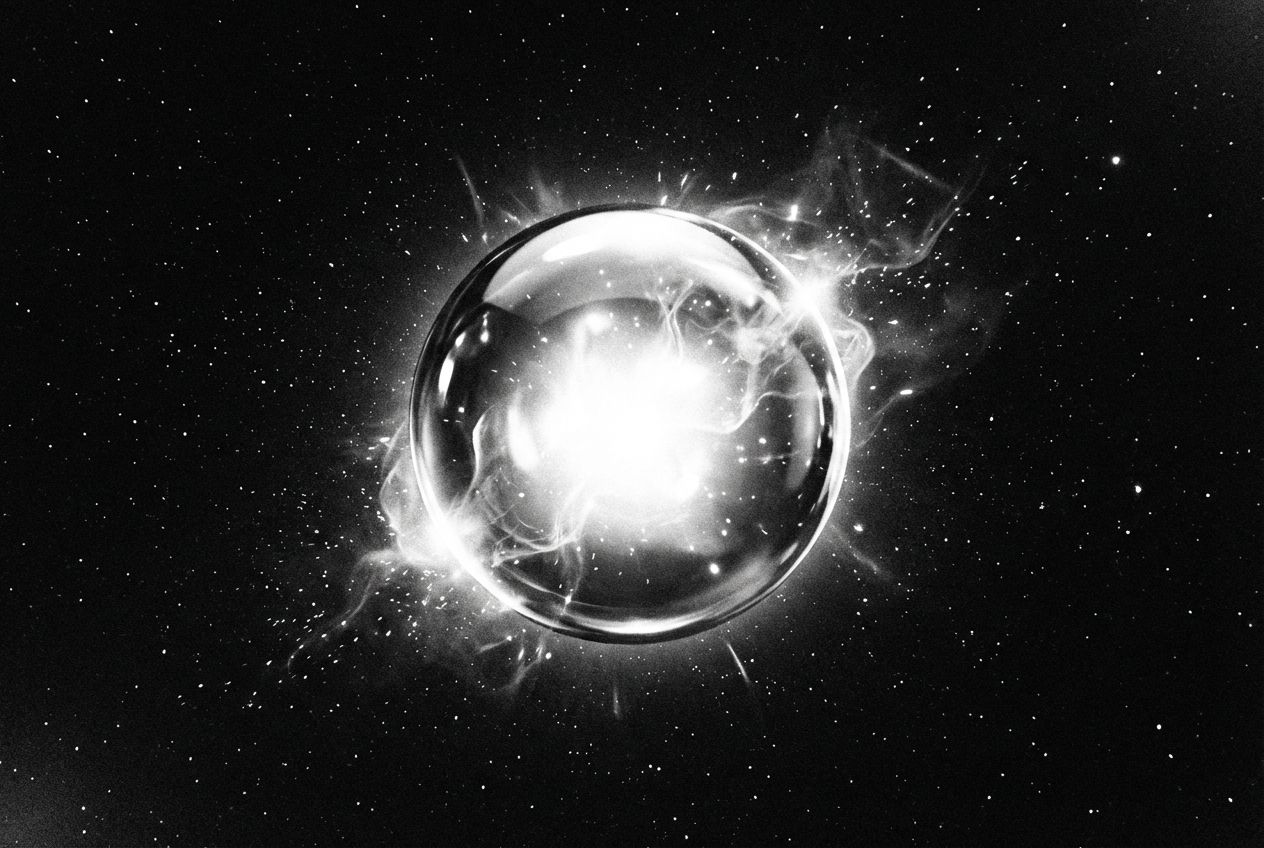 A dramatic, high-contrast photograph of a single, highly polished sphere, glowing with an intense internal light. From its surface, subtle ethereal wisps and tiny sparks of energy gently emanate into the dark, vast space around it, suggesting fundamental particles and their dynamic interactions. Composed for a 3:2 landscape frame.
