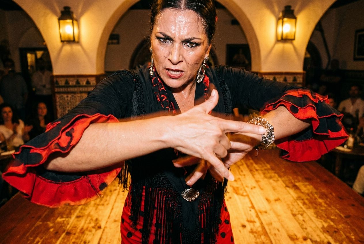 A dramatic, low-angle close-up photograph of a flamenco dancer mid-performance, captured in a moment of intense, sharp expression and powerful hand gesture. The focus is on the dancer's passionate movement, evoking the energy and precision of a quick, impactful response. Soft, warm stage lighting in a traditional Spanish tablao setting, 3:2 landscape.