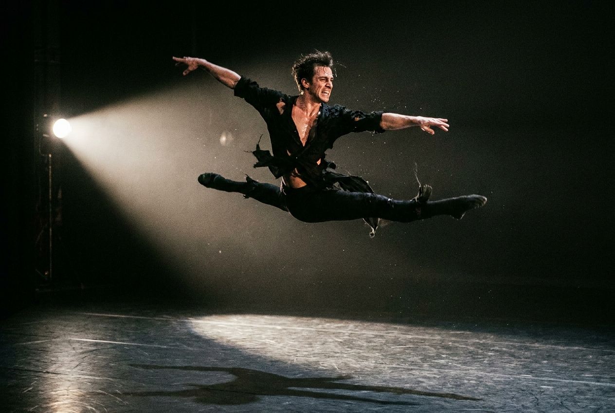 A powerful French ballet dancer in mid-air, caught in a dramatic leap across a darkened stage, illuminated by a single spotlight. The image conveys intense emotion and precision, composed as a vivid, striking photograph in a 3:2 landscape frame.